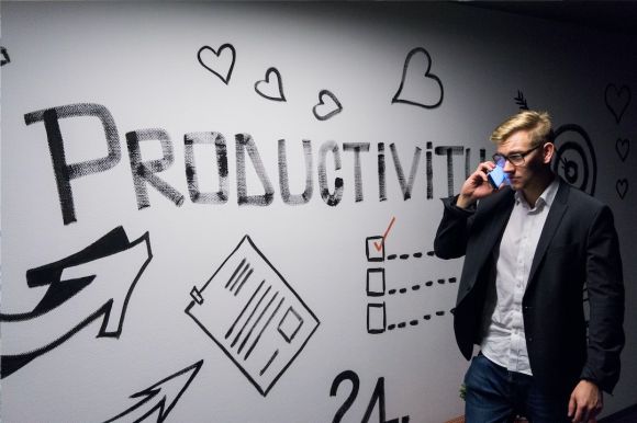 Enhanced Productivity - man holding smartphone looking at productivity wall decor