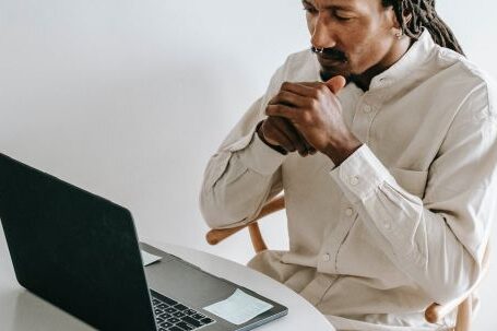 Programming - Concentrated adult African American male in formal wear sitting at table with cup of coffee and watching video on netbook in light room