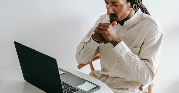 Programming - Concentrated adult African American male in formal wear sitting at table with cup of coffee and watching video on netbook in light room